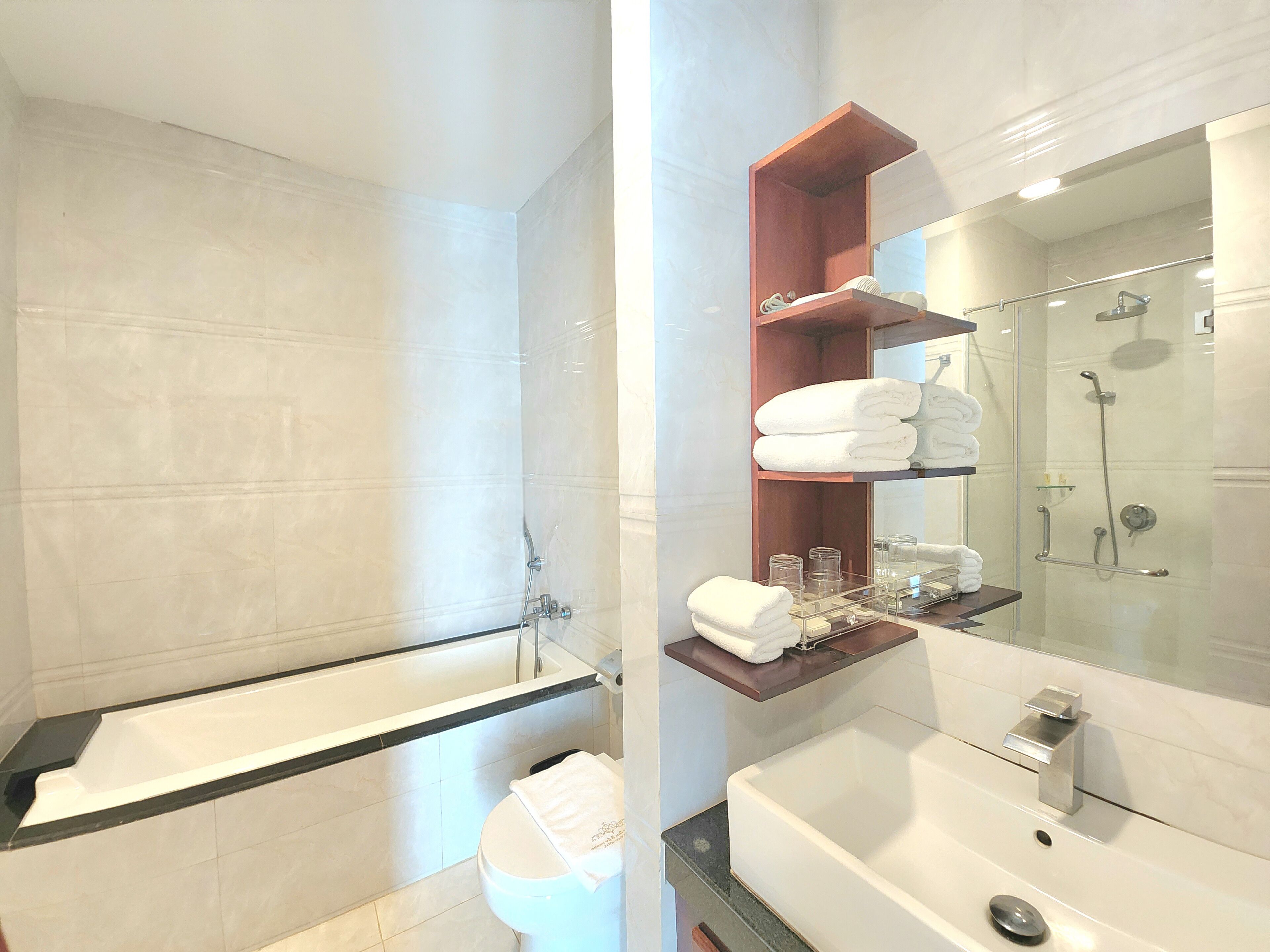 A modern bathroom with a bathtub, a shower, and a vanity with a mirror. There are shelves with towels and toiletries.