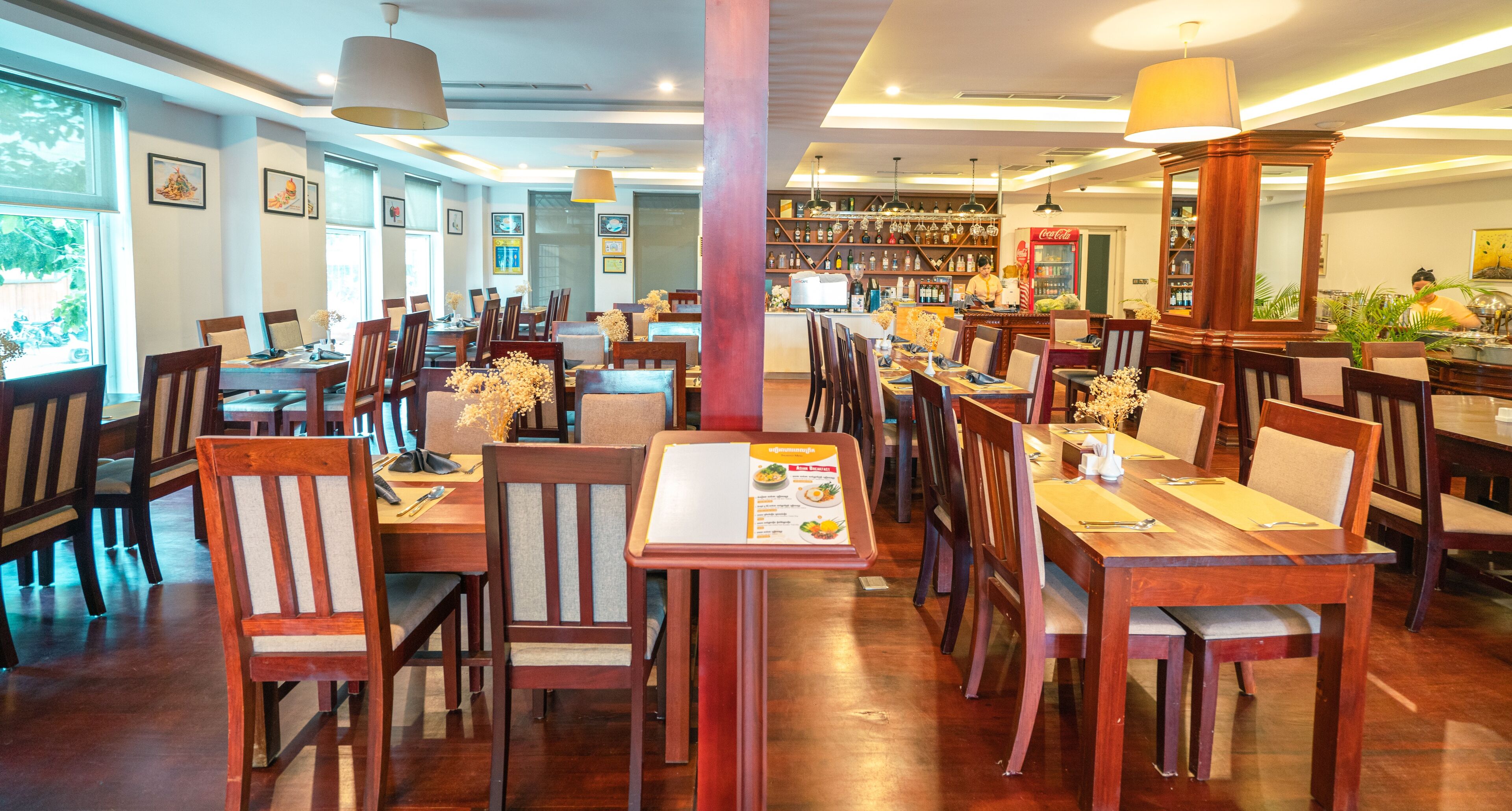 A restaurant with wooden tables and chairs, a bar area, and framed pictures on the walls.
