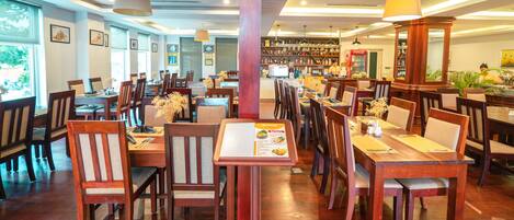 A restaurant with wooden tables and chairs, a bar area, and framed pictures on the walls.