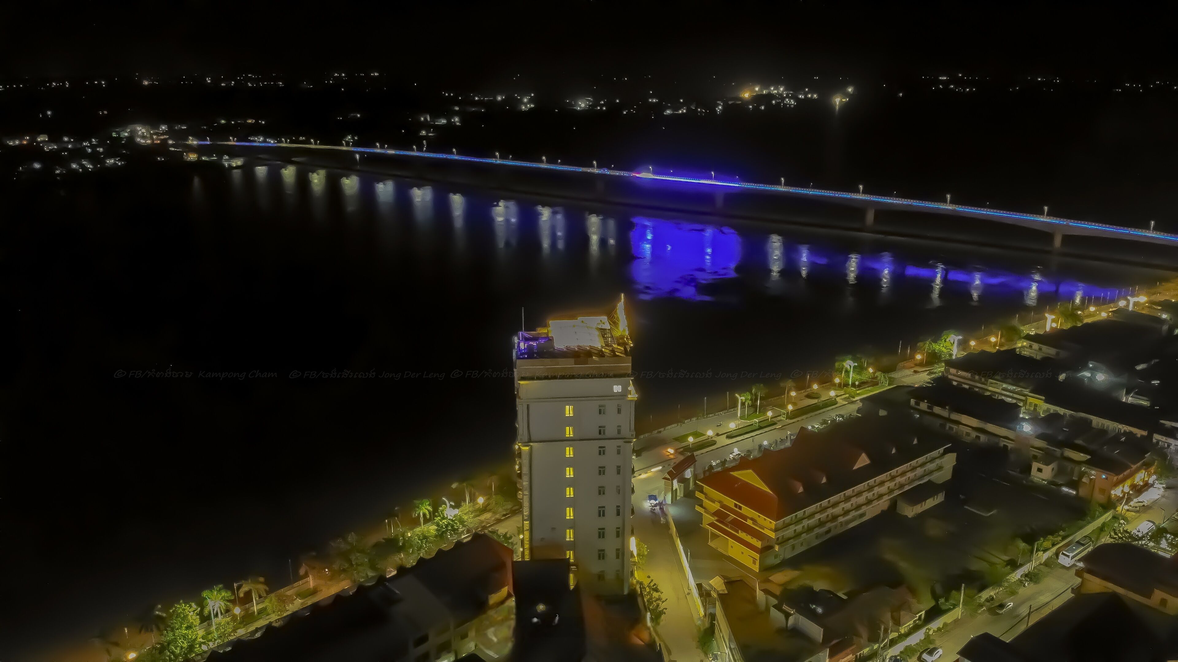 An aerial view of a cityscape at night with illuminated buildings, a bridge, and a river.