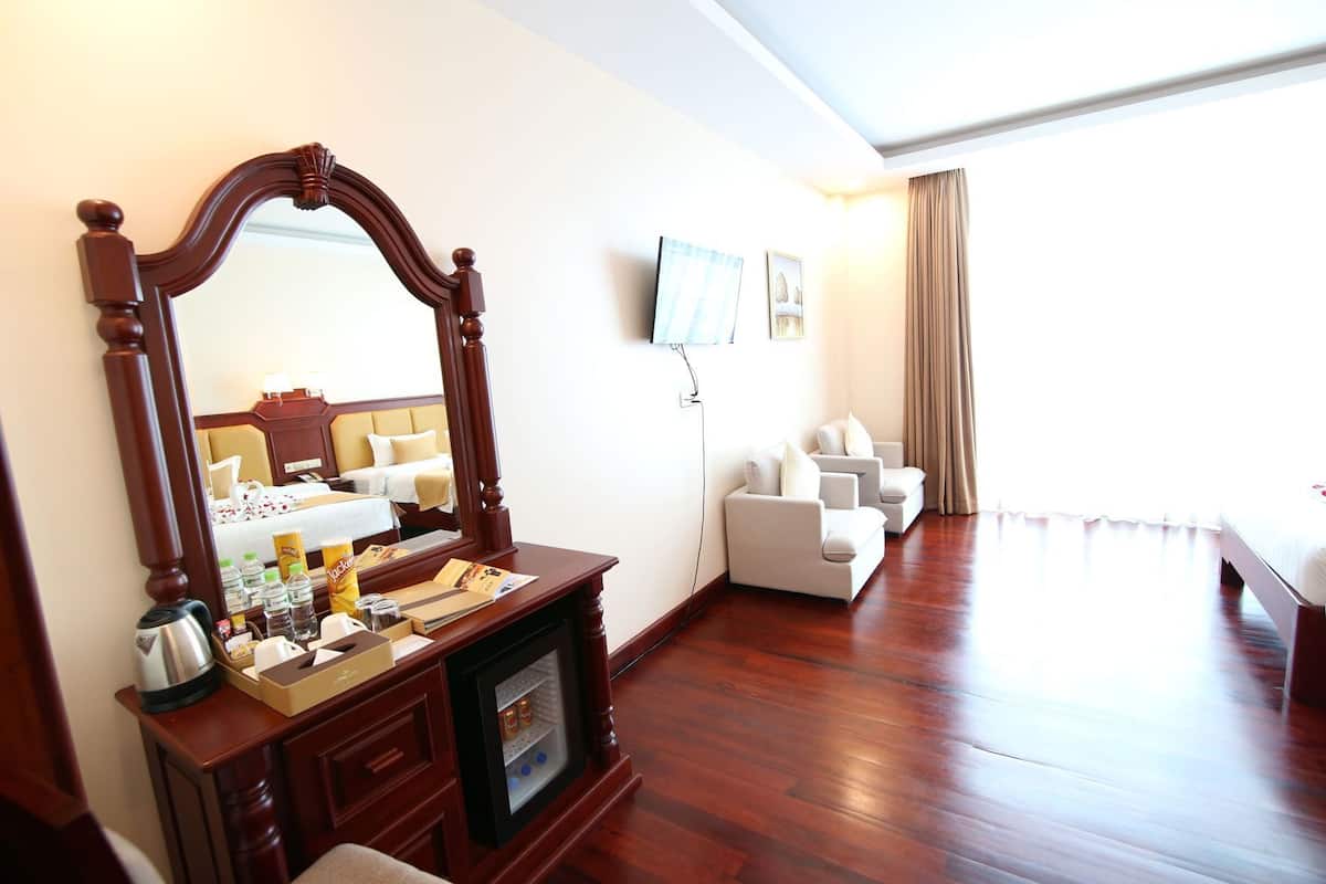 Une chambre d’hôtel avec une commode en bois, un grand miroir, une télévision, un canapé et un lit.