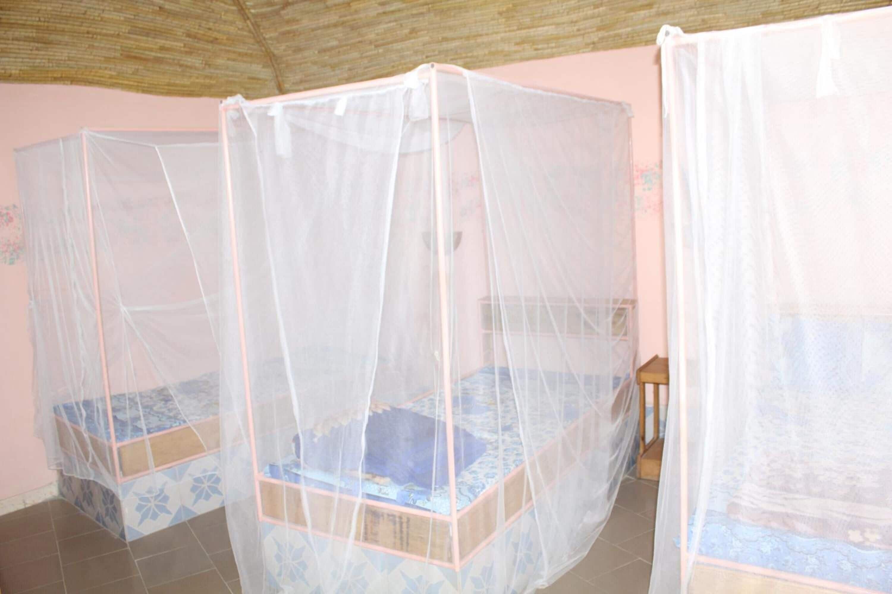 Two single beds with mosquito netting in a room with pink walls and a tiled floor.