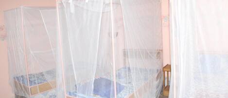 Two single beds with mosquito netting in a room with pink walls and a tiled floor.
