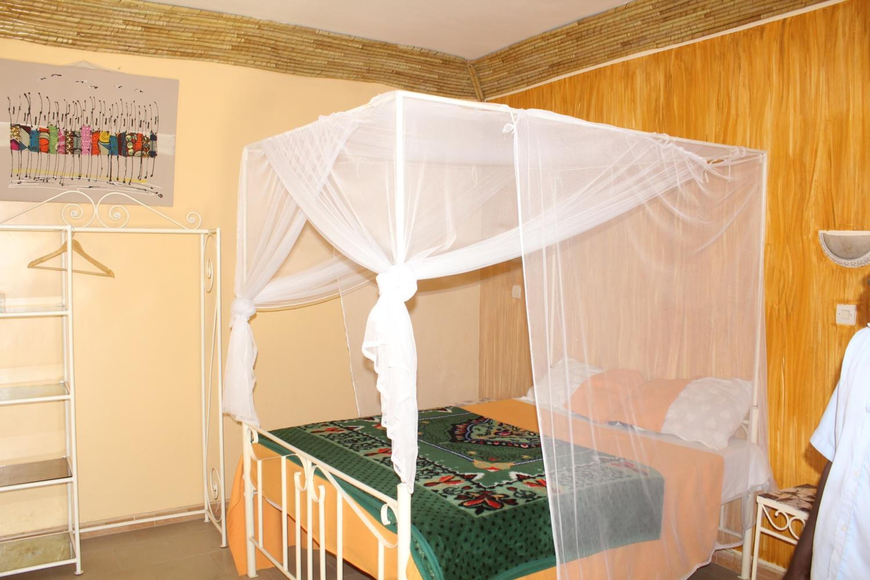 Una habitación con una cama bajo un dosel blanco, una pared de madera y un cuadro enmarcado.