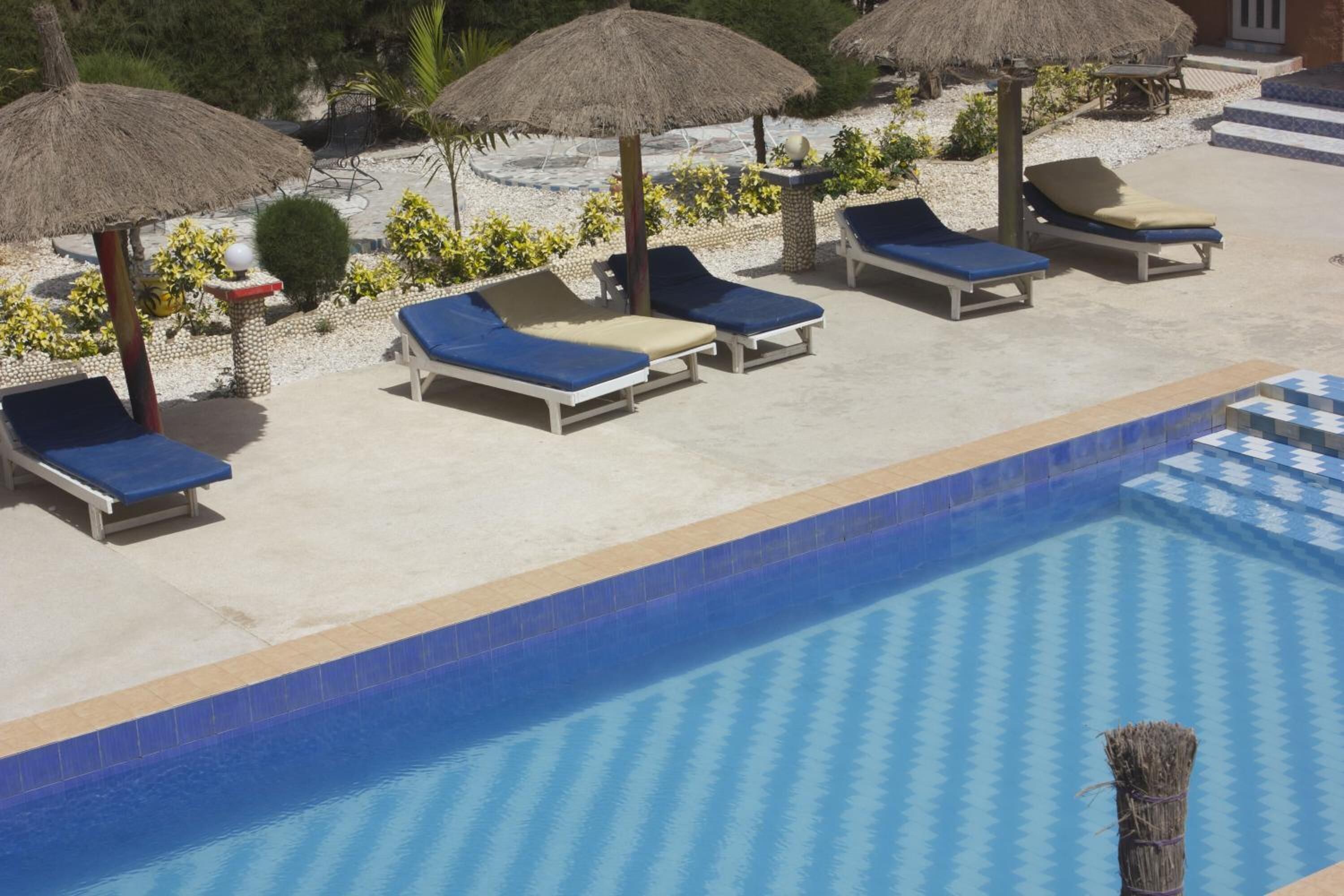 Un área junto a la piscina con sillones de descanso y sombrillas de paja.