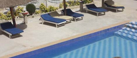 Un área junto a la piscina con sillones de descanso y sombrillas de paja.