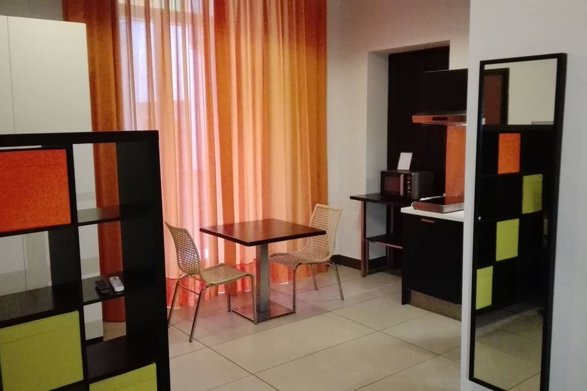 A small, compact room with a single table and two chairs, a bookshelf, and a mirror.