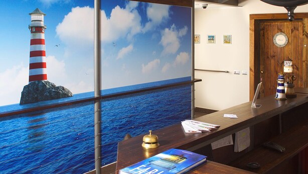 A reception desk with a view of the sea and a lighthouse, a wooden door, and a bell. - Residenza Pizzofalcone (Naples)