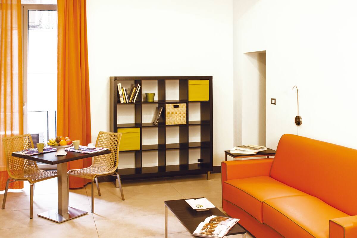A living room with a sofa, a dining table with chairs, a bookshelf, and a coffee table.