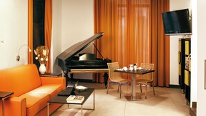 A living room with a grand piano, an orange sofa, a dining table with chairs, and a television mounted on the wall. - Residenza Pizzofalcone (Naples)