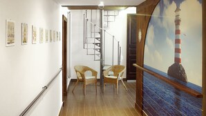 A hallway with a wooden floor, a spiral staircase, wicker chairs, and a painting of a lighthouse. - Residenza Pizzofalcone (Naples)