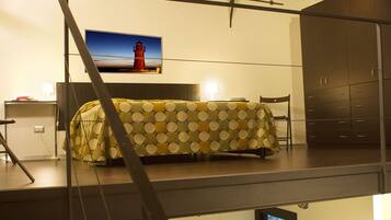 A bedroom with a bed covered in a polka dot blanket, a nightstand, a chair, and a wardrobe.