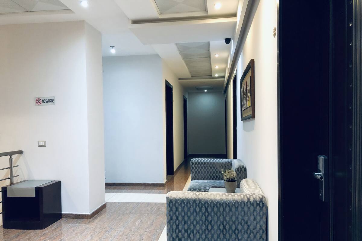 Un hall d’hôtel moderne, avec un panneau « interdiction de fumer », un coin salon doté de meubles recouverts d’un tissu à motifs et une porte sombre.