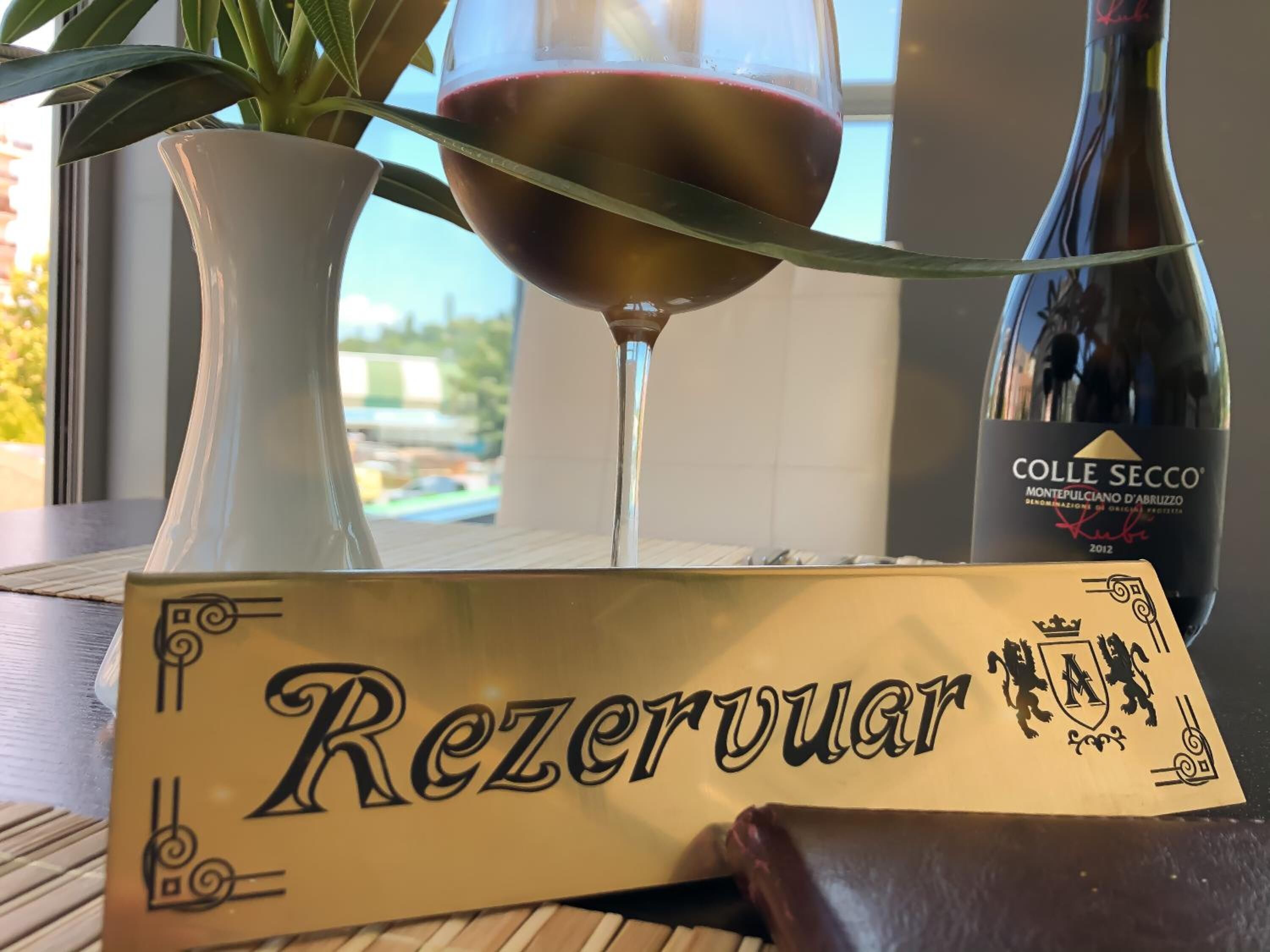 A bottle of Colle Secco wine, a glass of red wine, and a box labeled "Rezerwuar" on a table.