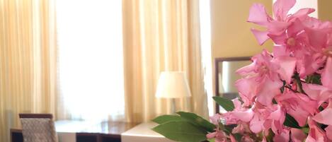A hotel room with a dining table, chairs, and a vase of pink flowers.