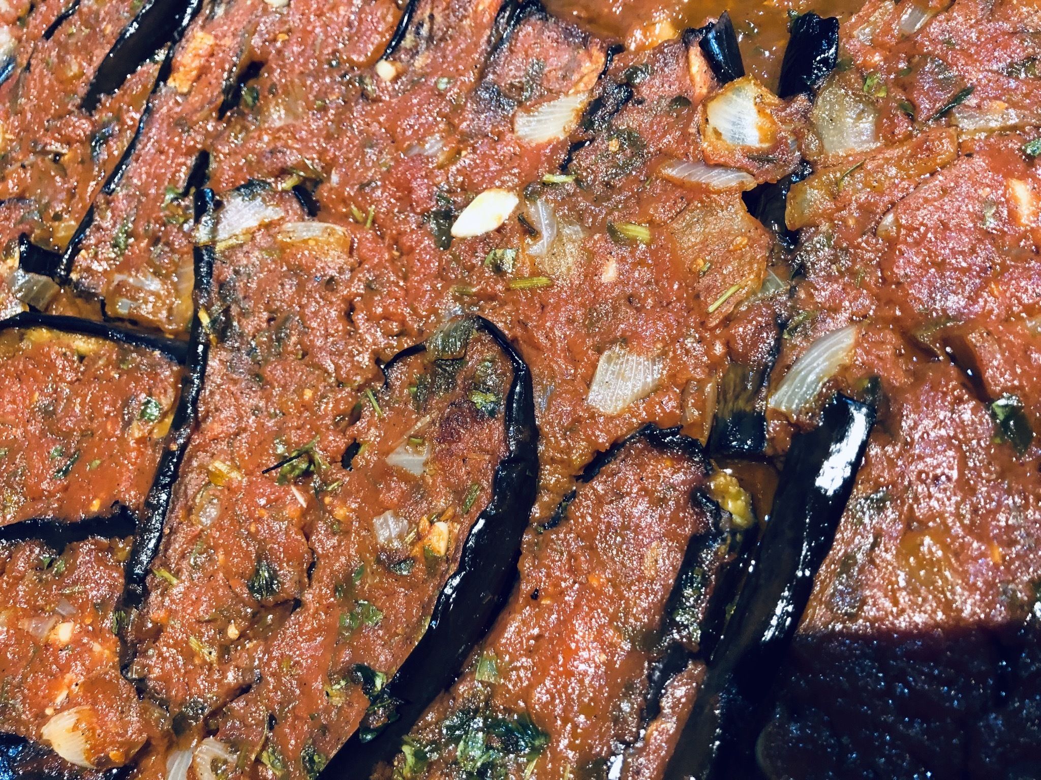 Een close-up van een bord met plakjes aubergine in tomatensaus, versierd met kruiden.