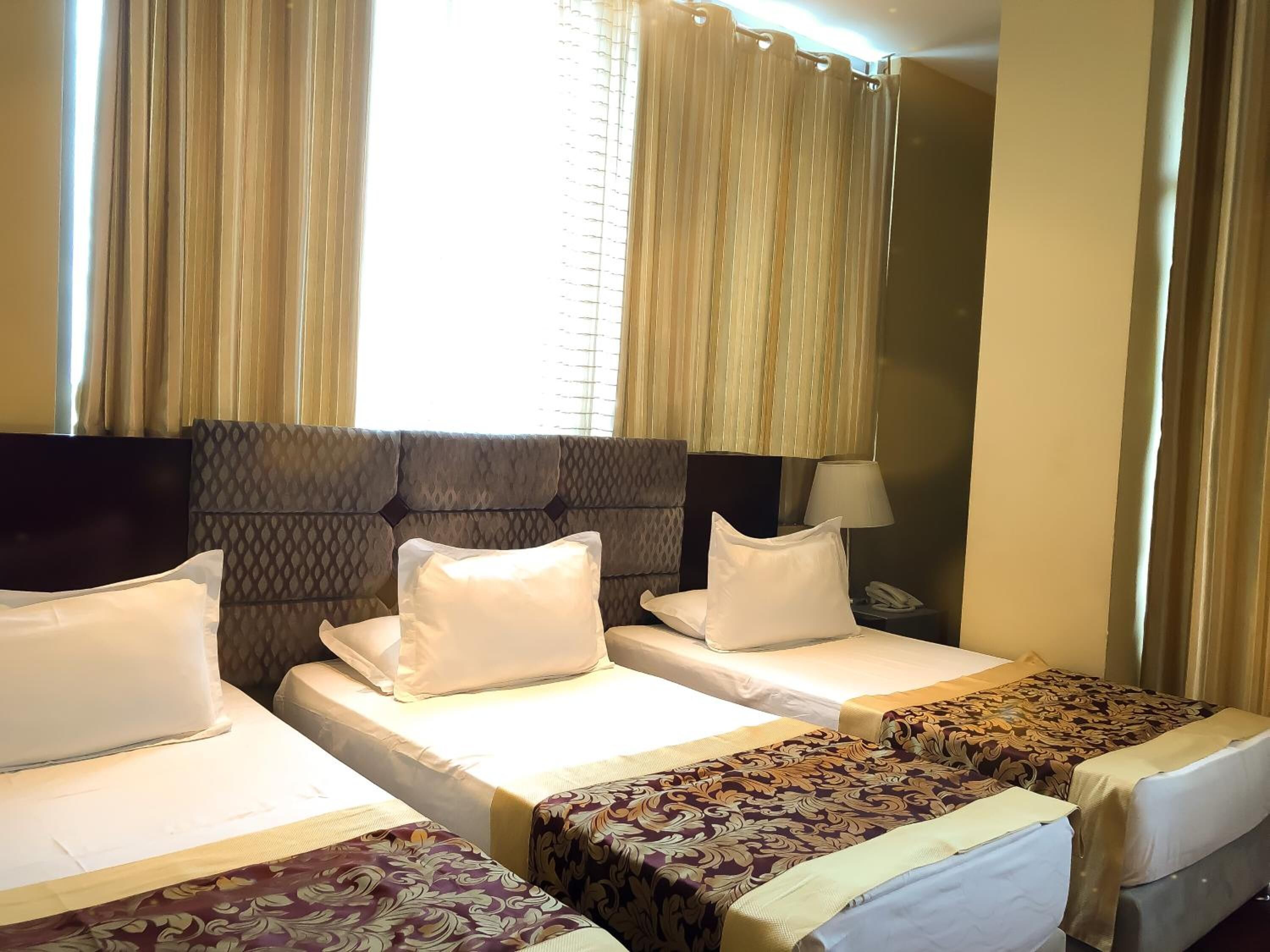 Quarto de hotel com duas camas de solteiro, uma cabeceira grande e uma janela com cortinas.