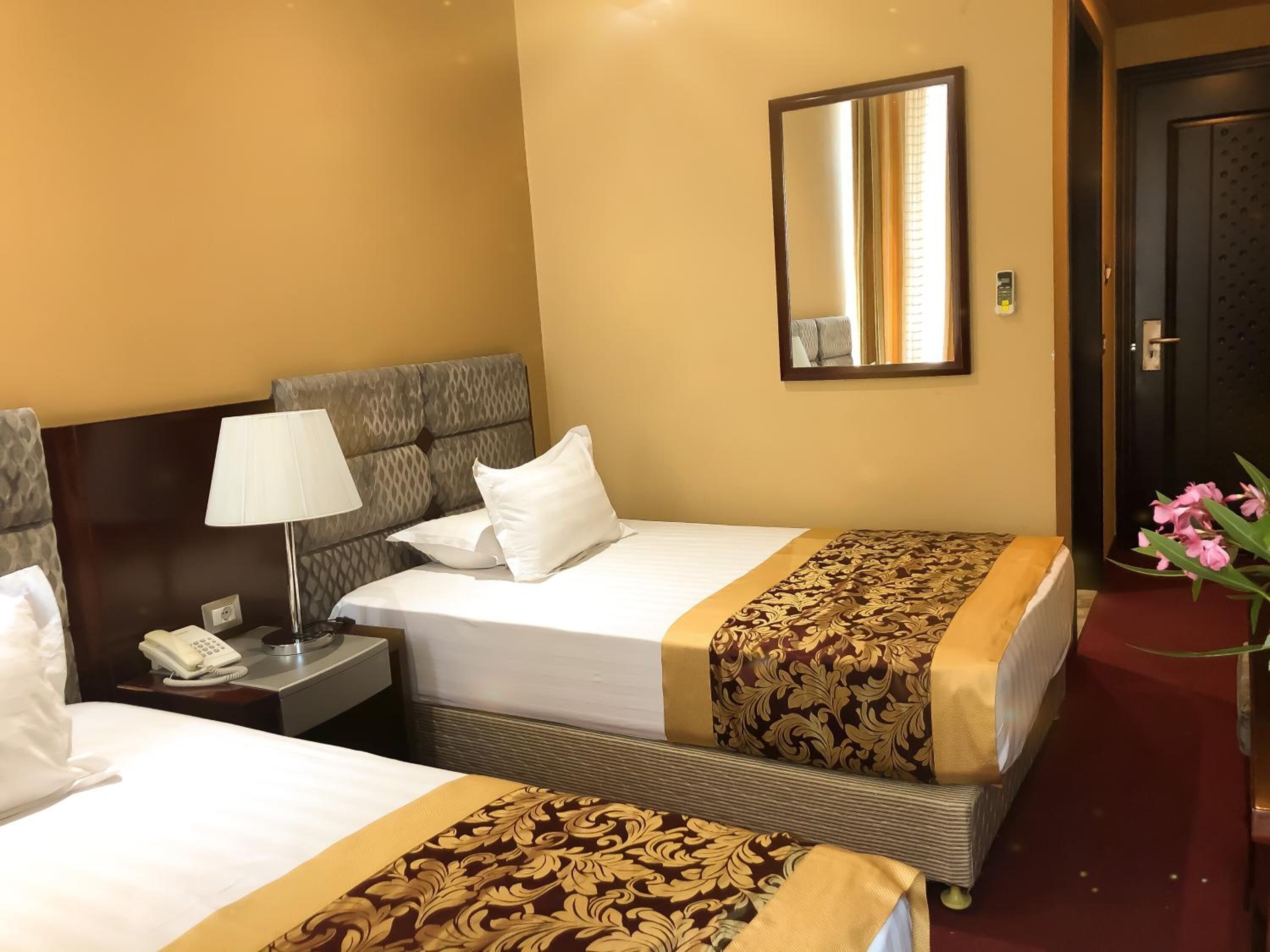 A hotel room with two beds, a bedside table with a lamp, a telephone, and a mirror on the wall.