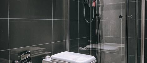 A modern bathroom with a glass-enclosed shower, a bidet, and a toilet.