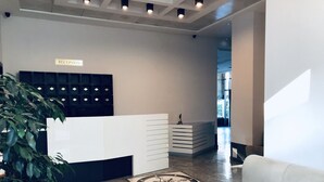 Un espace d’accueil comprenant un comptoir de réception blanc, une plante en pot, un tapis à motifs et un canapé de couleur claire.