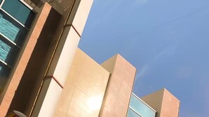 Un bâtiment moderne aux façades composées d’un mélange de panneaux beige et bleu clair, doté de grandes fenêtres et surplombant un ciel dégagé.