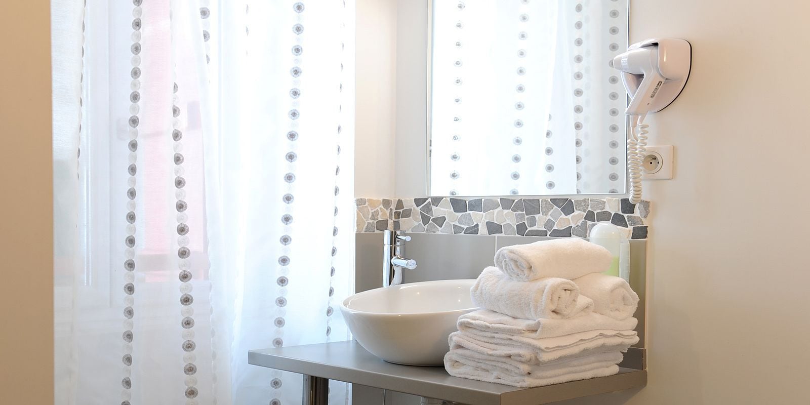 A bathroom with a white sink, a mirror, a hairdryer, and a stack of towels.