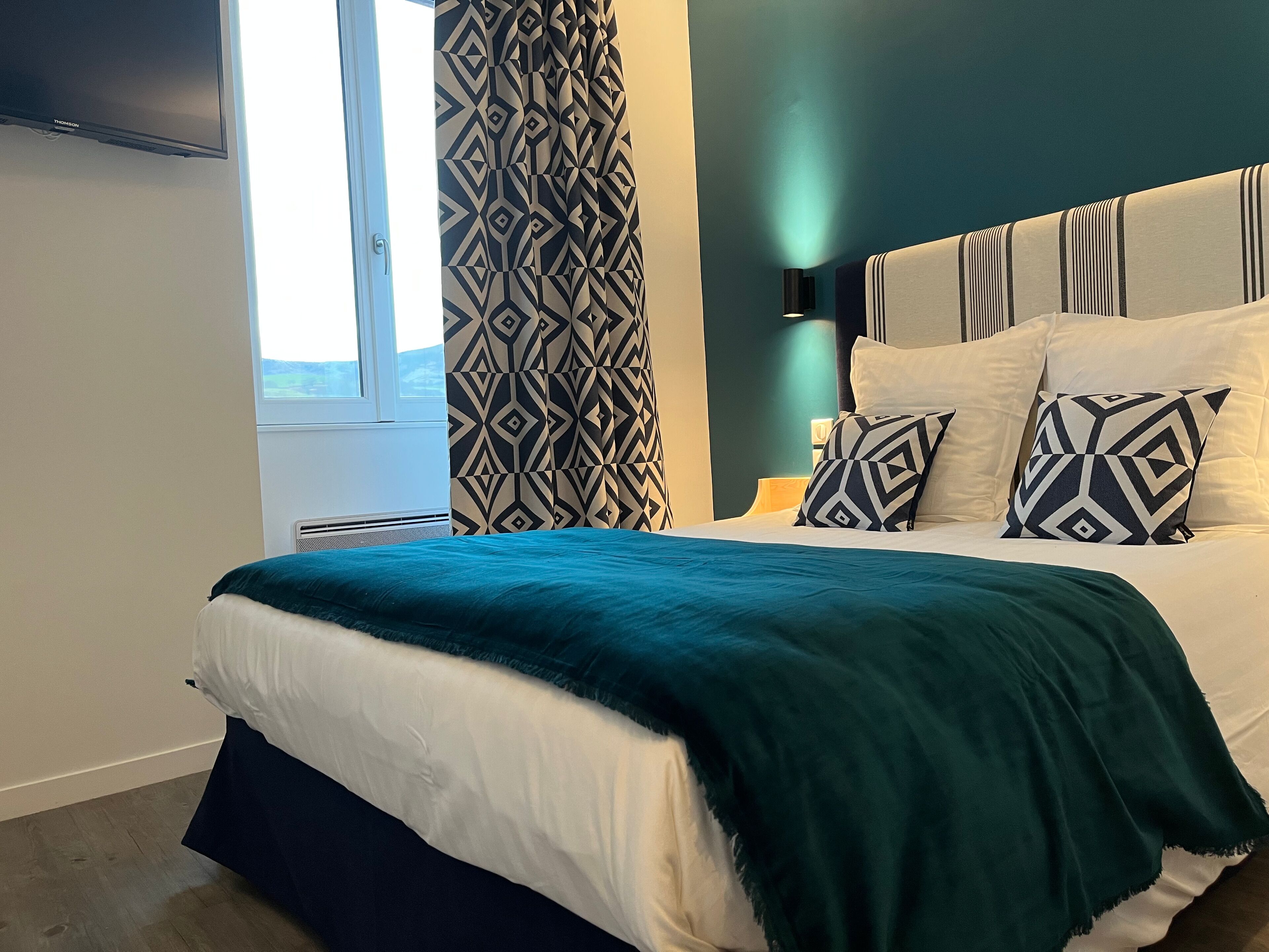 A modern bedroom with a bed, patterned curtains, and a nightstand with a lamp.