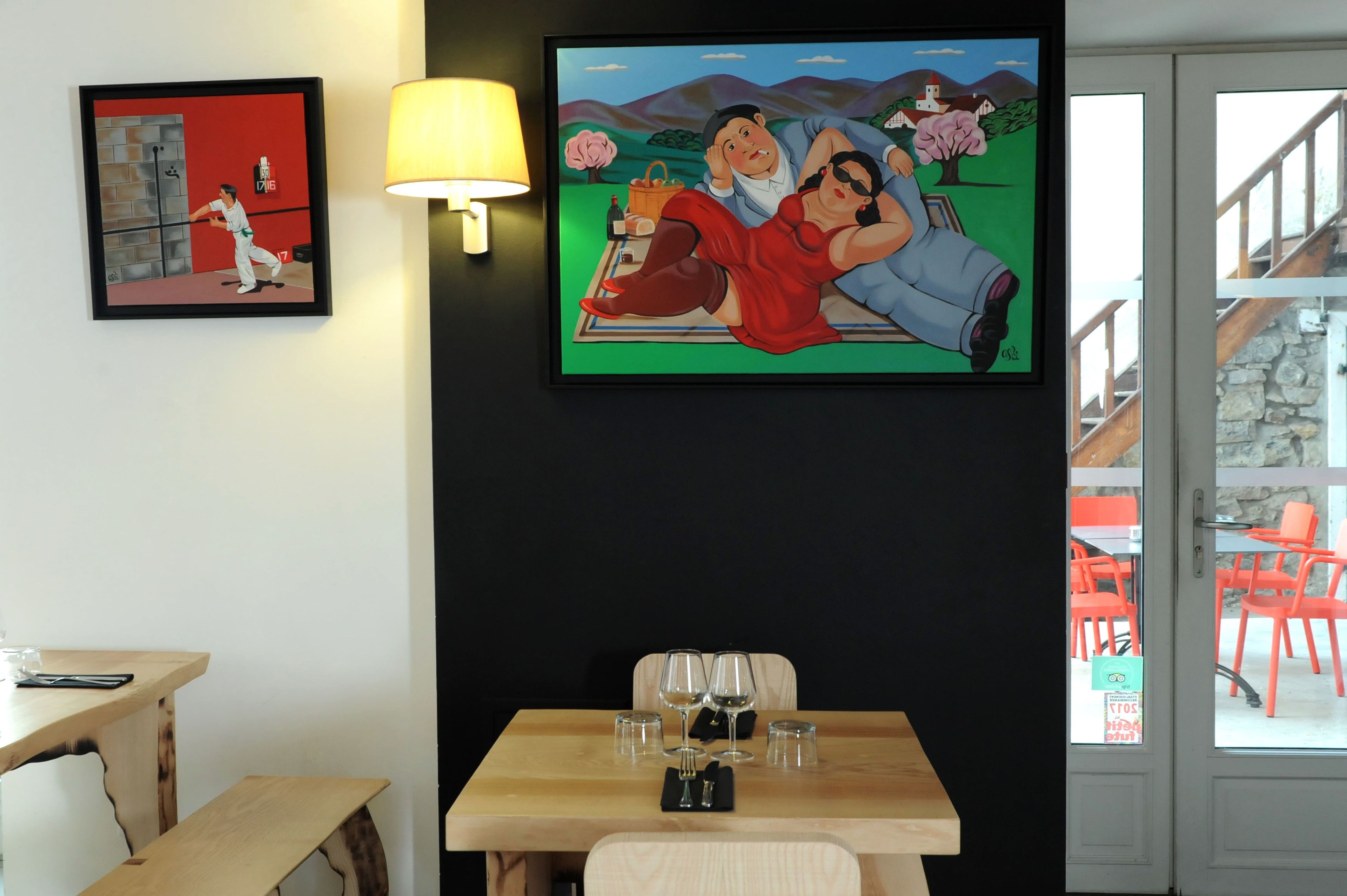 A room with a dining table set for two, a TV mounted on the wall, and a framed picture above the table.