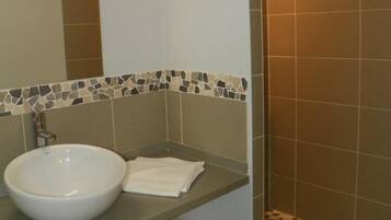 Ein Badezimmer mit einem weißen Waschbecken, einem Spiegel und einer Duschkabine mit Mosaikfliesen.