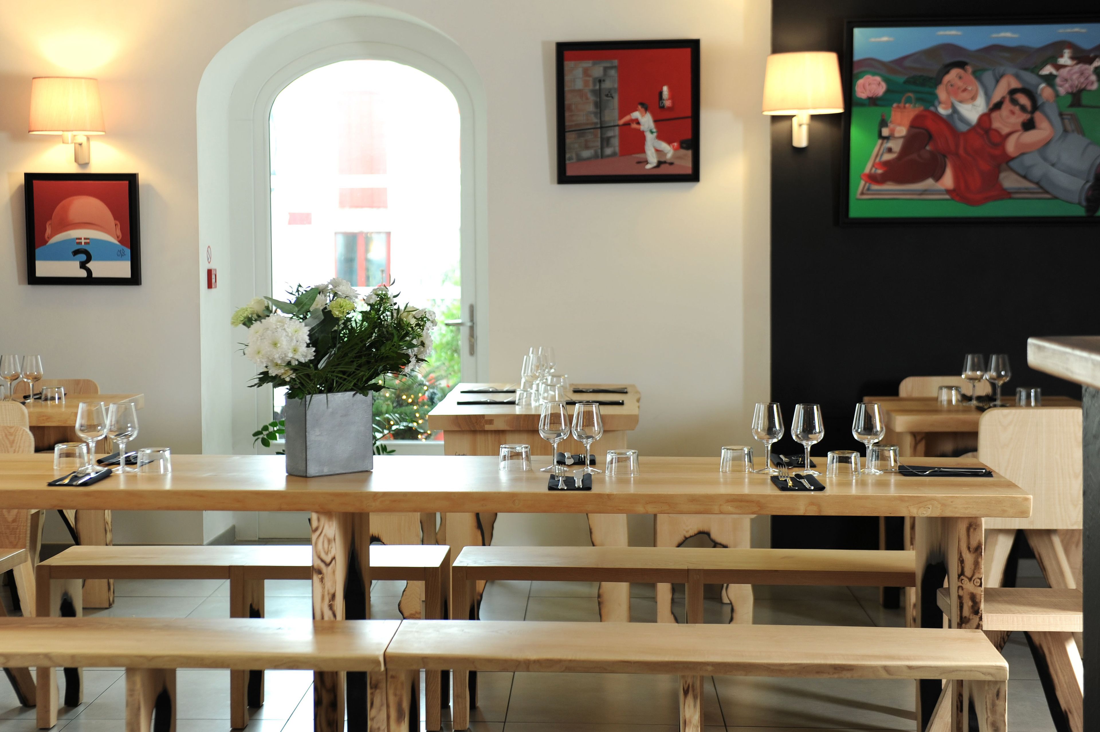 Un restaurante con mesas y bancos de madera, un jarrón de flores y obras de arte en las paredes.