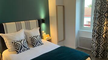 A bed with a geometric-patterned pillow, a bedside table with a lamp, and a window with patterned curtains.