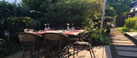 Un patio exterior con una mesa lista para comer, rodeado de abundante follaje y una terraza de madera.