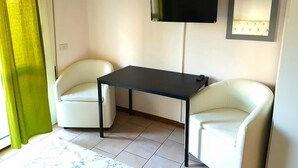 A room with two white armchairs, a small black table, a flat-screen TV mounted on the wall, and a lighted mirror. - Nightstars B&B (Mestre)