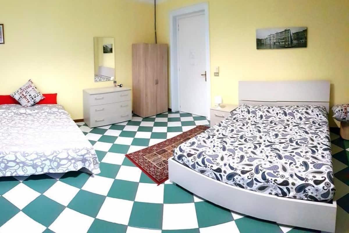 A room with two beds, a wardrobe, a mirror, and a checkered floor.