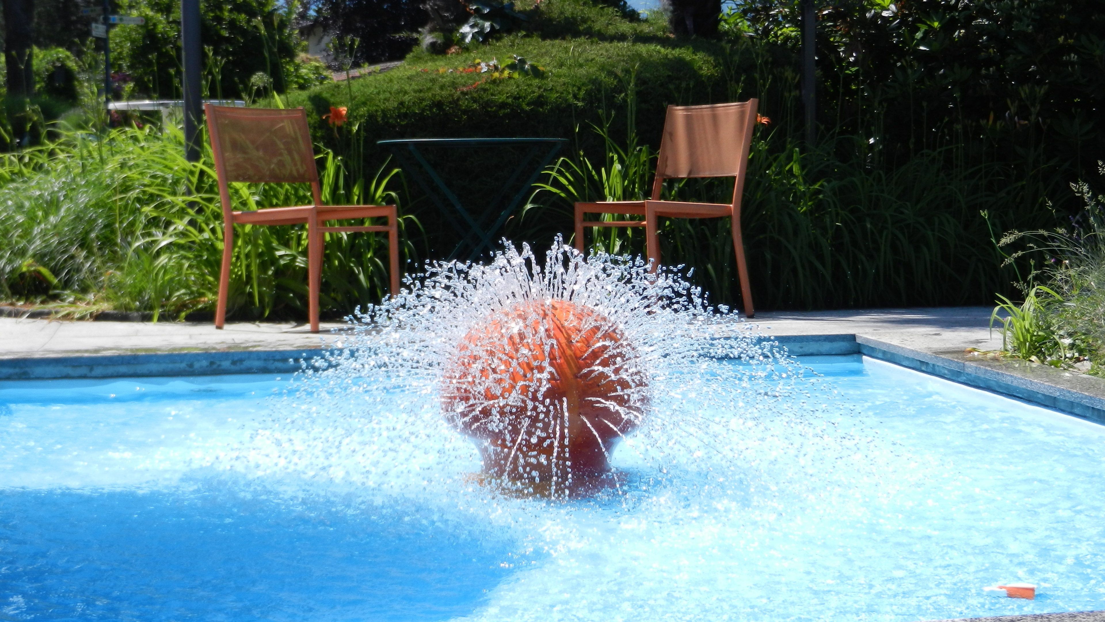 Une piscine où l’eau éclabousse, entourée de chaises et de verdure.