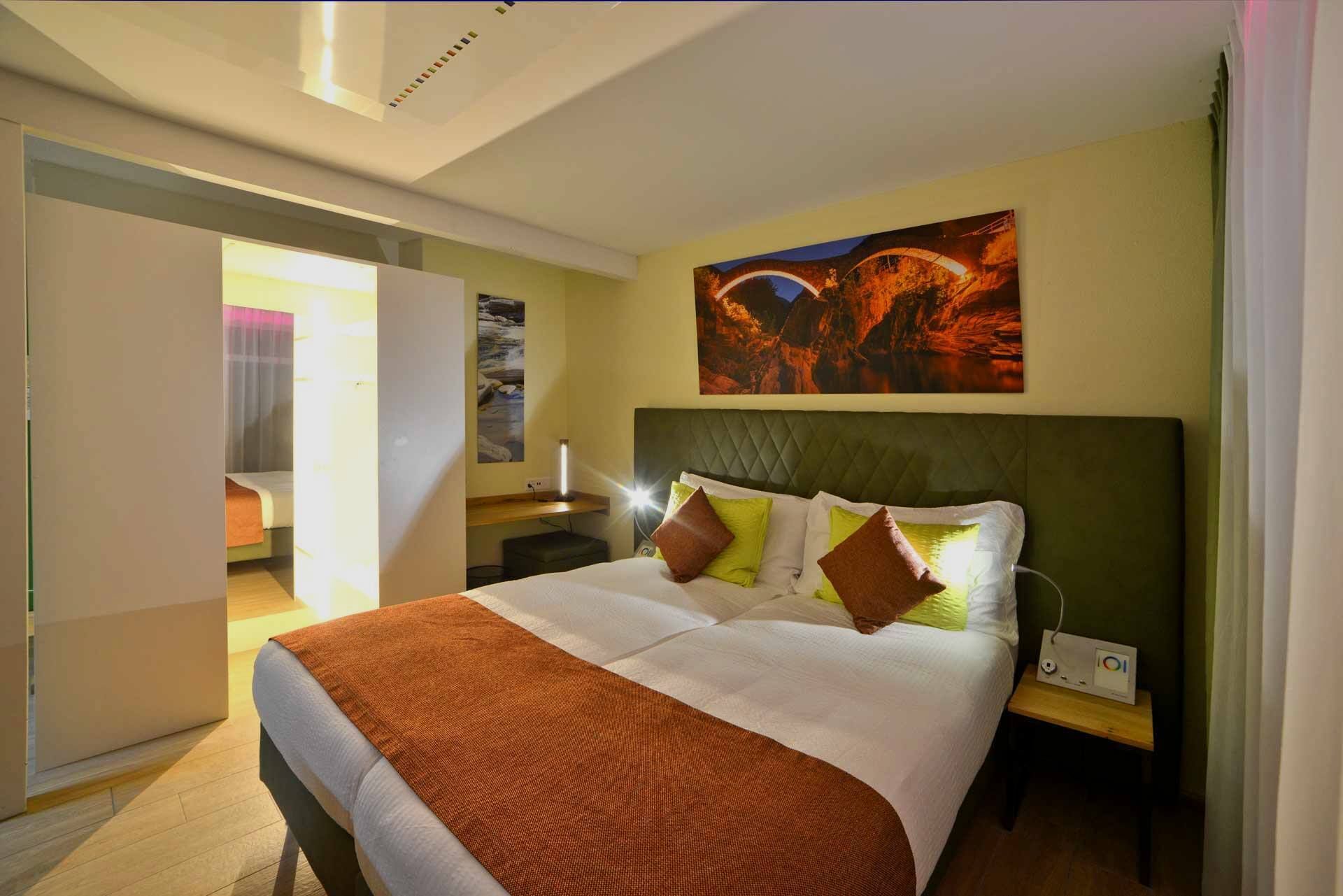 Une chambre d’hôtel avec un grand lit, une table de chevet, une lampe fixée au mur et un tableau au-dessus du lit.