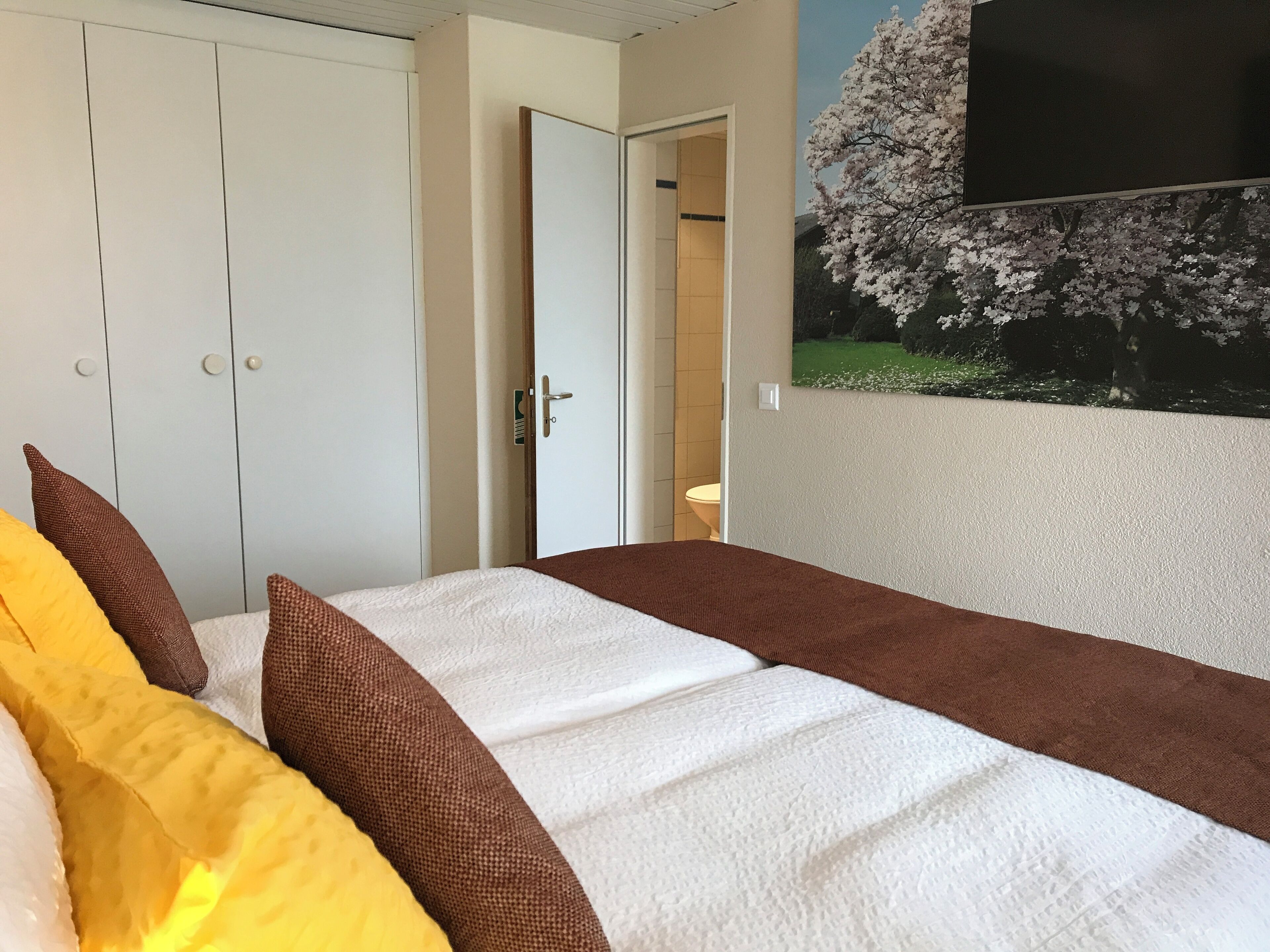 Une chambre à coucher avec un lit, des oreillers, une armoire et un tableau représentant un arbre.