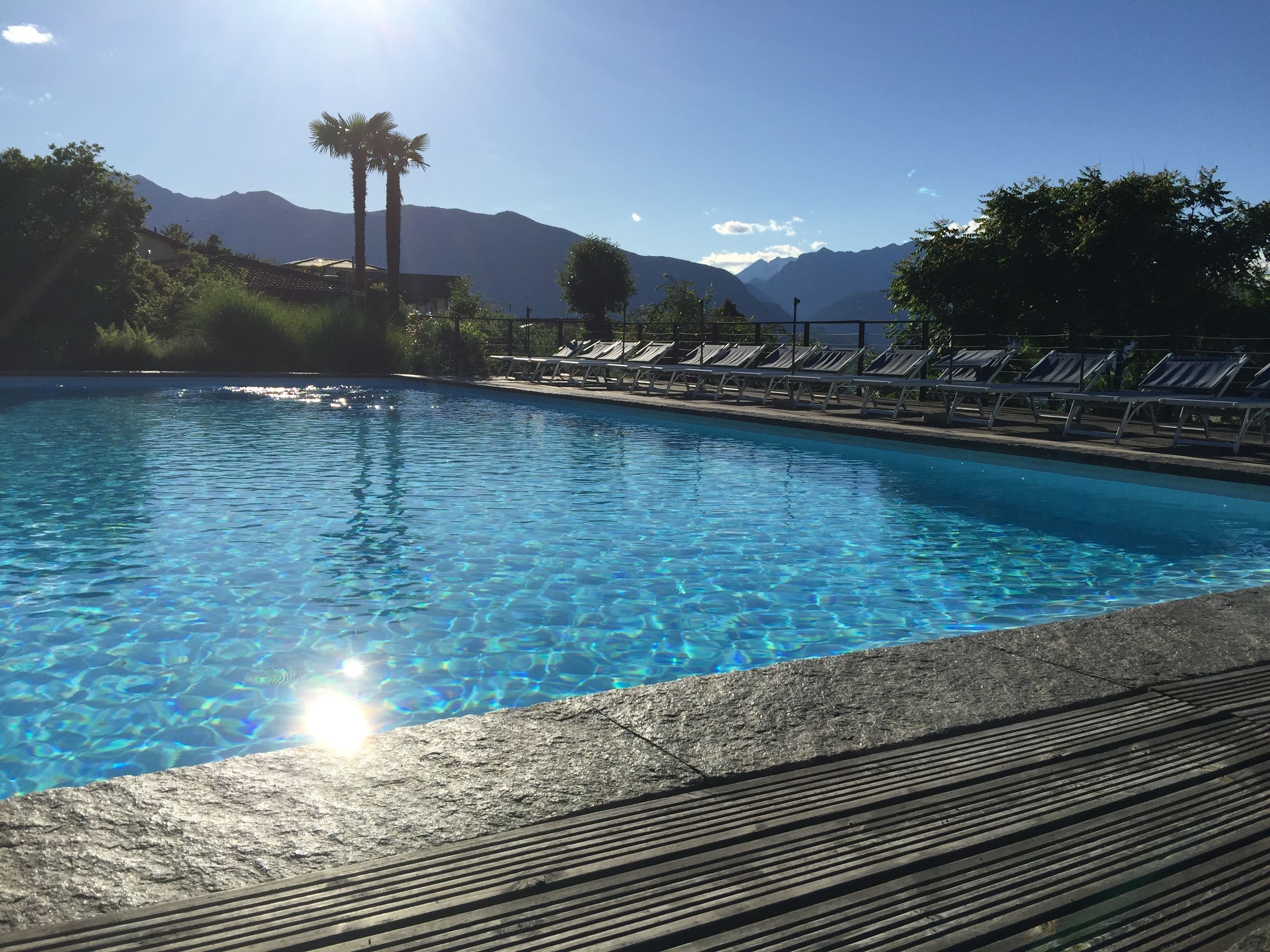 Una piscina cristalina con sillas de descanso y montañas al fondo.