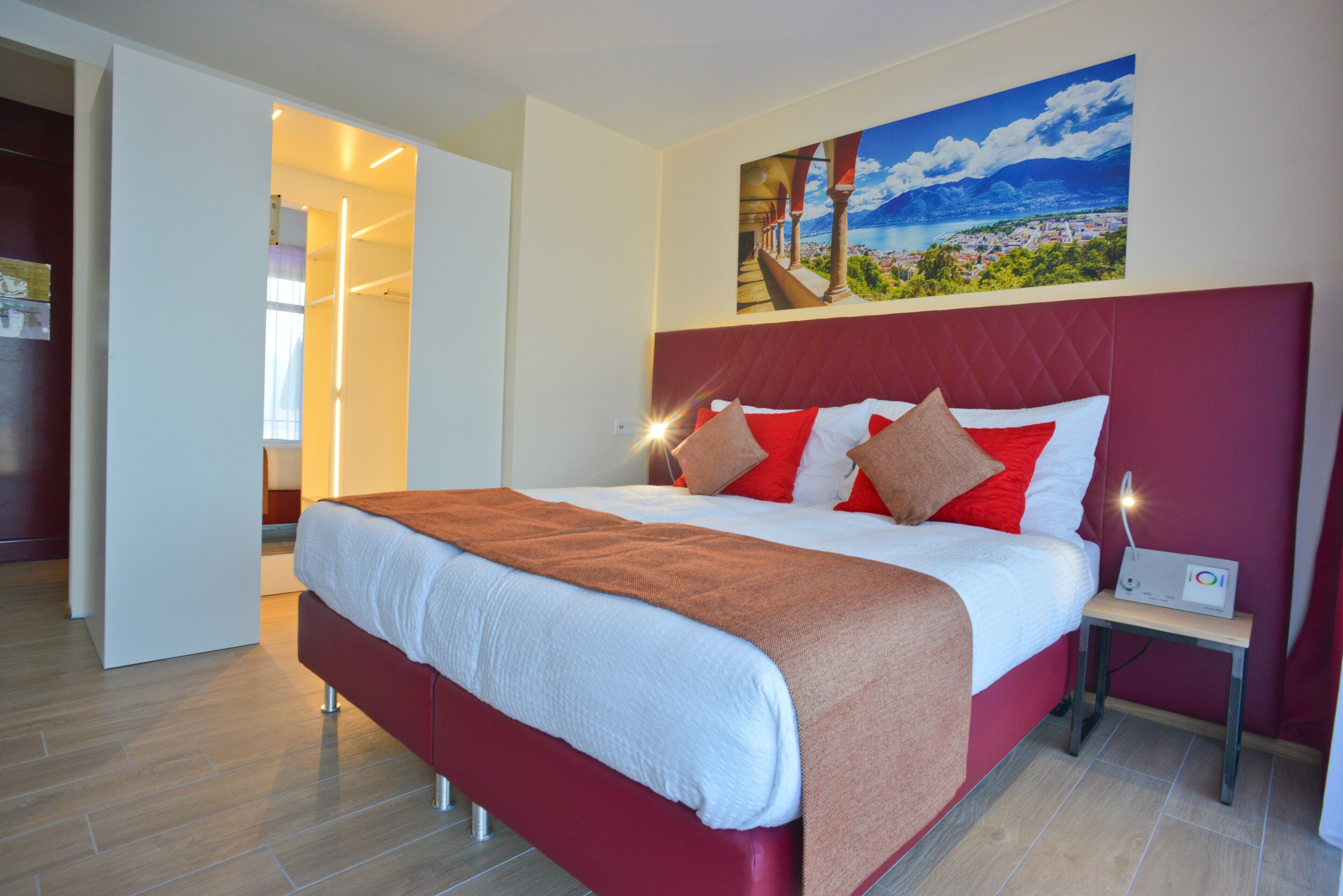 A modern hotel room with a large bed, a painting of a coastal landscape, and a bedside table with a lamp.