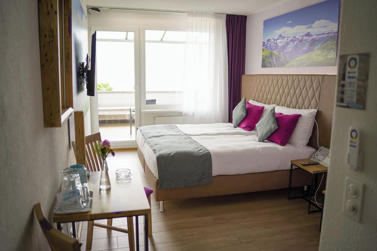 Een hotelkamer met een bed, een tafel met een karaf en glazen, een stoel en uitzicht op de omgeving.