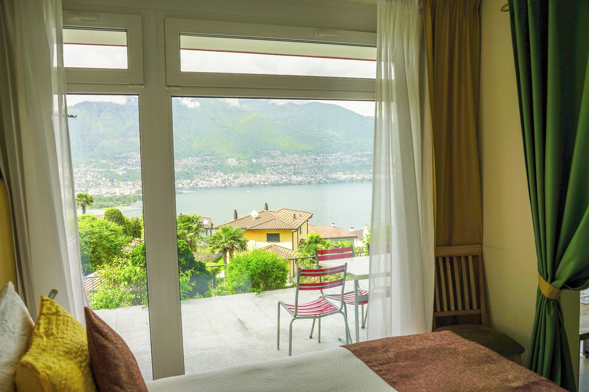 A room with a large sliding glass door leading to a balcony with a view of a lake and houses.