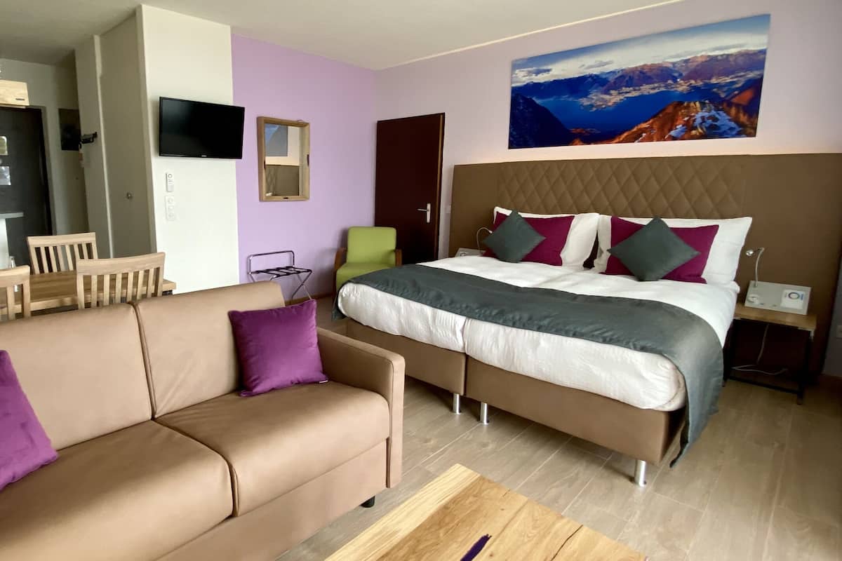 Een moderne hotelkamer met een bed, een bank, een tafeltje, een televisie, een schilderij en een stoel.