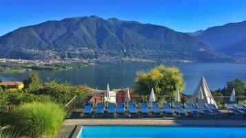 Una piscina con sillas de descanso y vistas a un lago y montañas.