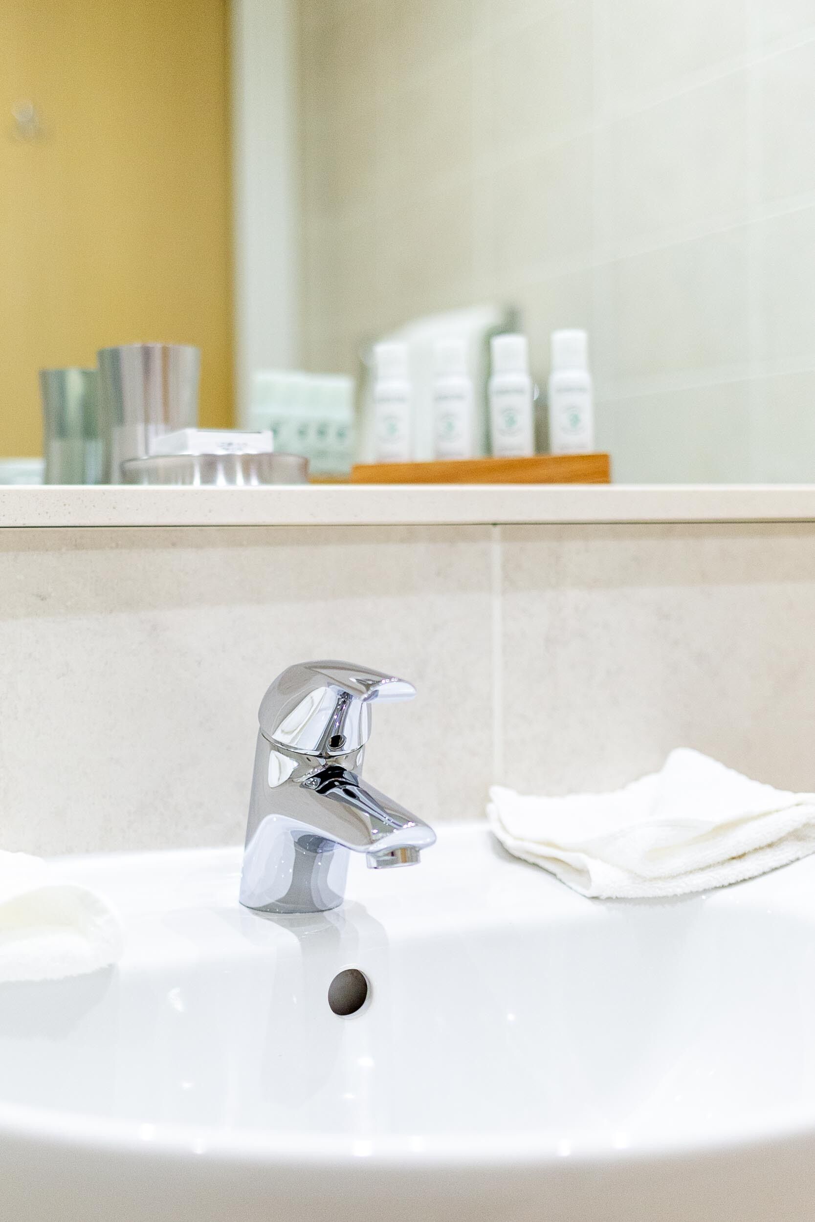 Un lavabo de salle de bain avec un robinet chromé, une serviette blanche et des articles de toilette rangés sur une étagère.