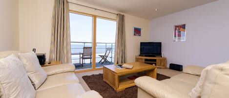 A modern living room with a sofa set, a coffee table, a TV, and a balcony with a view.