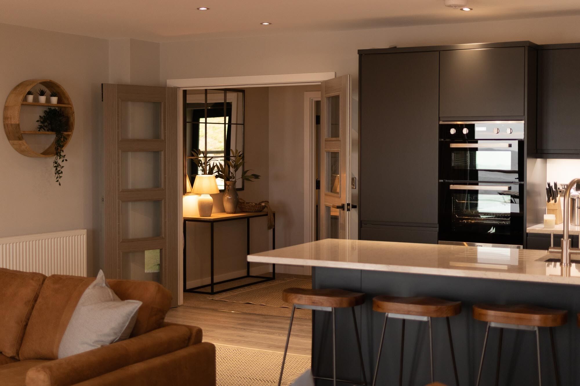 A modern kitchen with a central island, dark cabinetry, and a built-in oven.