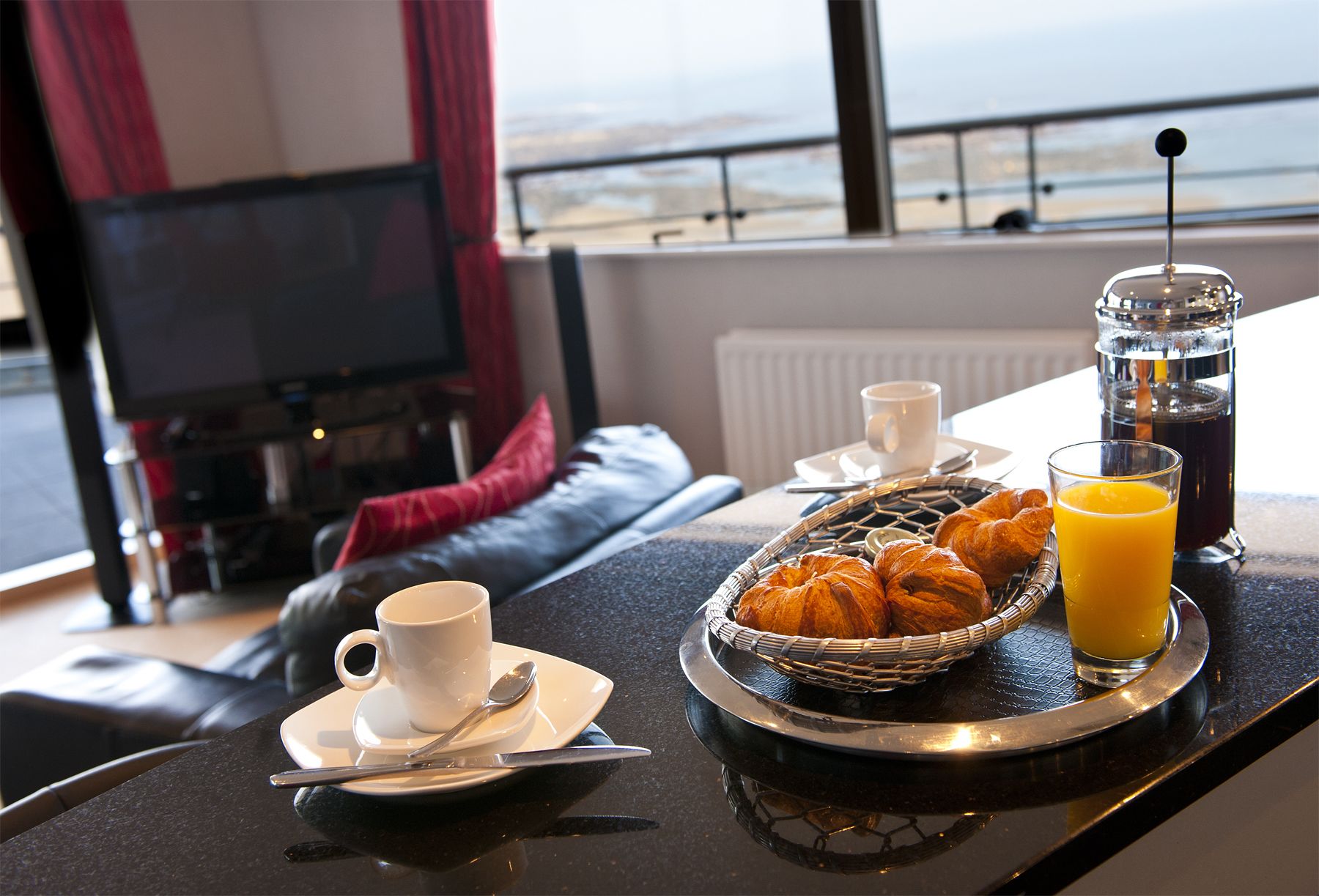 Ein Frühstücksbrett mit Croissants, einer Kaffeetasse und einem Glas Orangensaft auf einem Tisch mit Meerblick.