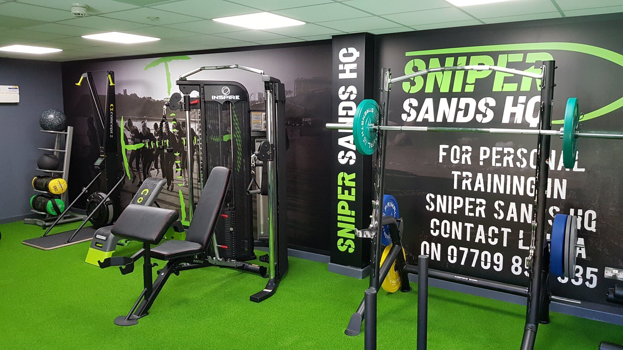 A gym with various exercise equipment, a green carpet, and a wall with text advertising personal training services.