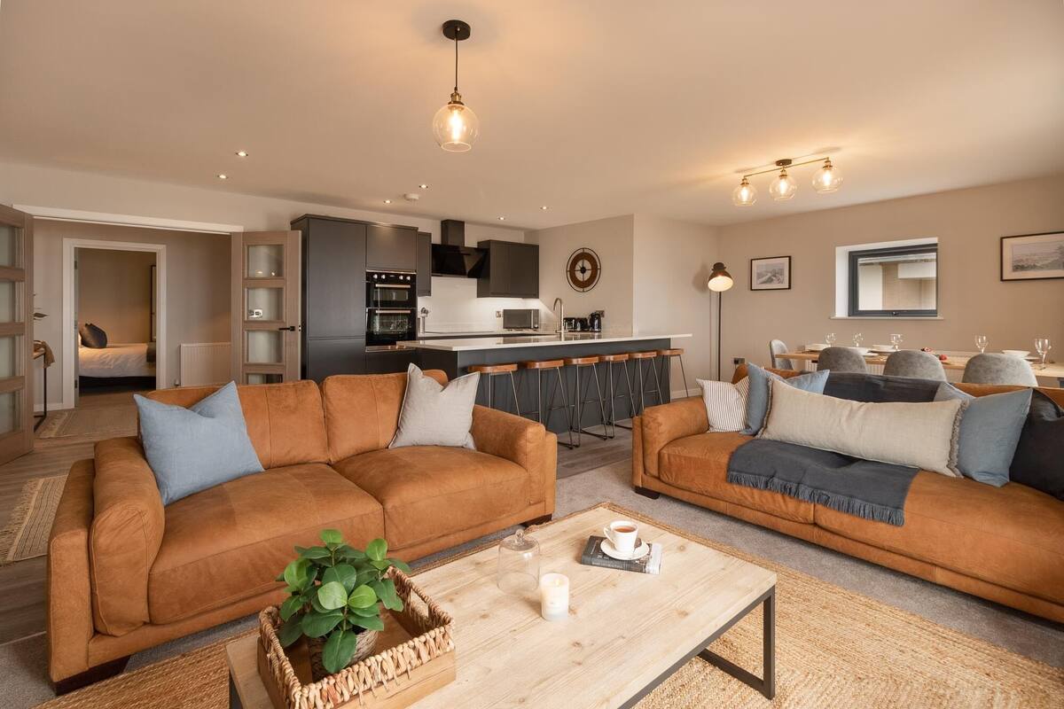 A modern living room with two sofas, a coffee table, and a kitchen in the background.