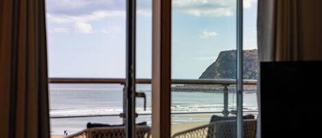 Une chambre avec une grande fenêtre donnant sur la plage, et comprenant une chaise et une table.